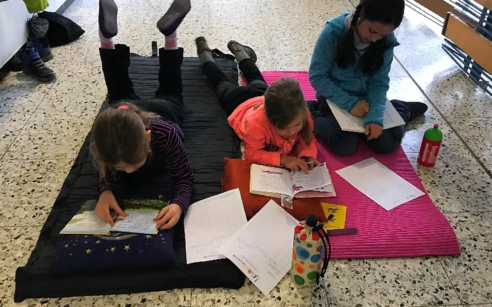 Begeistert Lesen die Schüler der Anne-Frank-Schule | © UNICEF/Ursula Grass Lesen für UNICEF: Die Schülerinnen haben sich zum Lesen auf Matten bequem gemacht