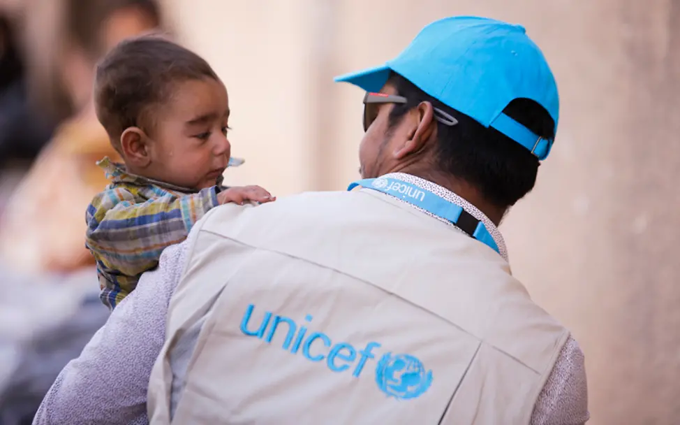 Ein UNICEF-Mitarbeiter trägt in den Syrien den 6 Monate alten Yusuf | © UNICEF/Sanadiki Syrien: Ein UNICEF-Mitarbeiter trägt einen Jungen