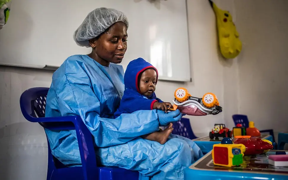 Ebolaimmune Pflegerinnen versorgen die Kinder in Ebolazentren. | © UNICEF/Tremeau Ebola bekämpfen: Eine Ebolaüberlebende in Ebola-Schutzkleidung spielt mit einem Baby.