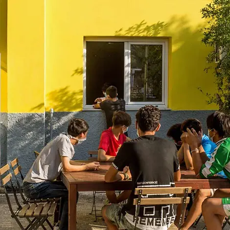 Nach dem Großbrand in Moria können die Jugendlichen in der Notunterkunft entspannen. | © UNICEF/Christophilopoulos Mehrere geflüchtete Jugendliche sitzen zusammen im Hof des Kinderzentrums an einem Tisch.