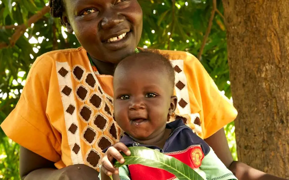 Akot spielt mit einem Mangoblatt | © UNICEF/Wilson Akot sitzt auf dem Schoß seiner Mutter und spielt vergnügt mit einem großen Blatt.