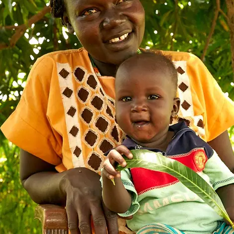 Akot spielt mit einem Mangoblatt | © UNICEF/Wilson Akot sitzt auf dem Schoß seiner Mutter und spielt vergnügt mit einem großen Blatt.