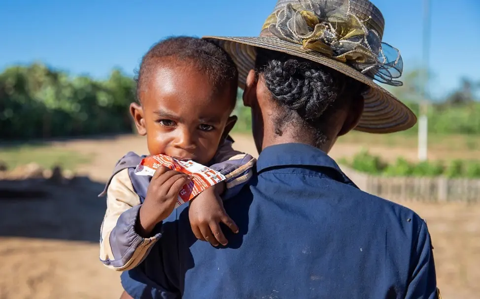 Schwere Mangelernährung | © UNICEF/Ralaivita Madagaskar: Kind auf dem Arm der Mutter hält Erdnusspaste in der Hand