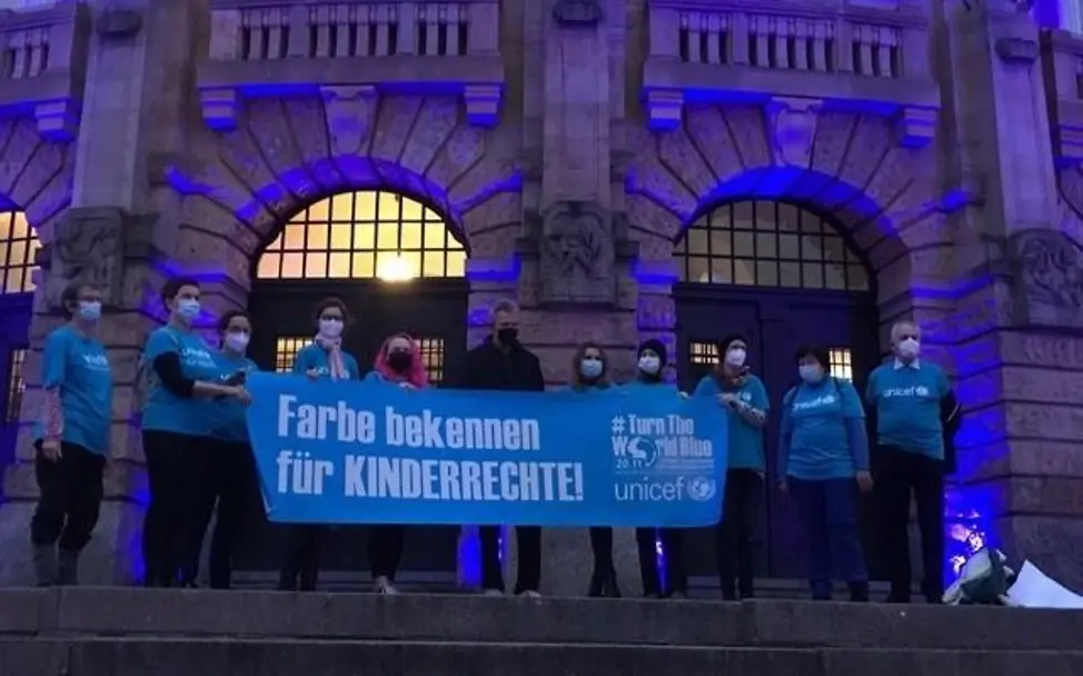 Tag der Kinderrechte 2021 | © Petra Tröndle Freiburg: UNICEF engagierte halten ein Plakat zum Tag der Kinderrechte vor dem blau erleuchteten Theater hoch.