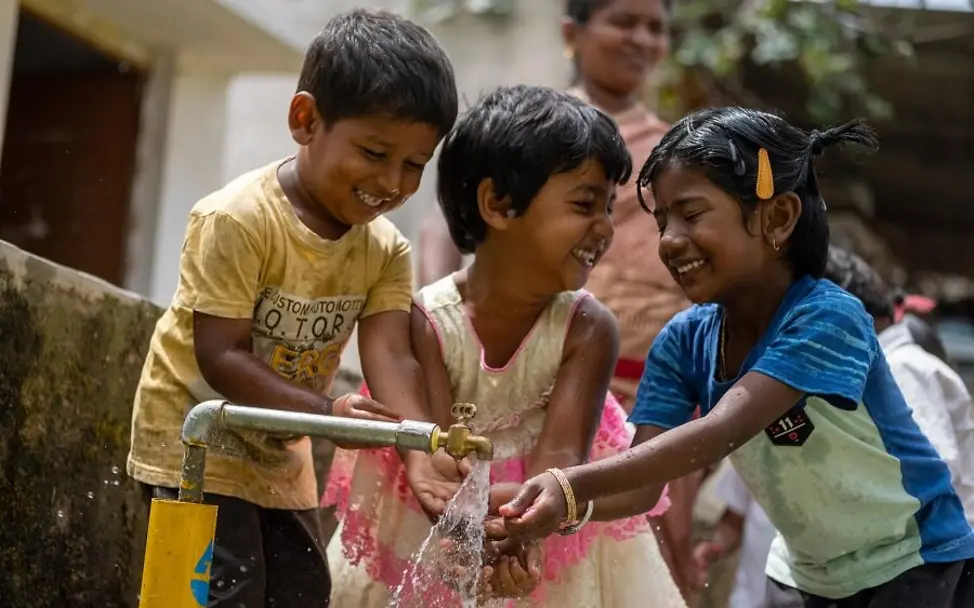 Klimawandel: So sprechen Sie mit Kindern darüber. | © UNICEF/Muthuramalingam Klimawandel für Kinder erklärt: Drei Kinder waschen sich im Freien die Hände.