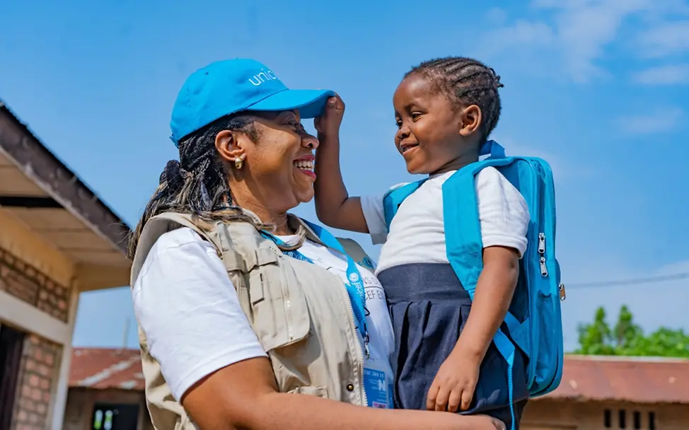 DR Kongo: Die 7-jährige Nkembo wird von UNICEF-Mitarbeiterin im Arm gehalten, nachdem er ein UNICEF-Schulpaket erhalten hat | © UNICEF/UNI456462/Mulala Weltflüchtlingstag: DR Kongo: Die 7-jährige Nkembo wird von UNICEF-Mitarbeiterin im Arm gehalten.