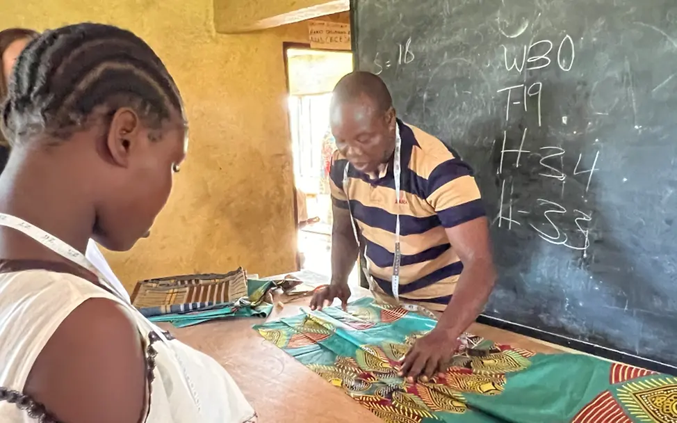 Mohammed Konneh bringt den Jugendlichen in Logan Town bei, wie sie Maß nehmen und Röcke oder Hemden passend anfertigen | © UNICEF/Bücker Mohammed Konneh breitet Stoff auf seinem Tisch aus.