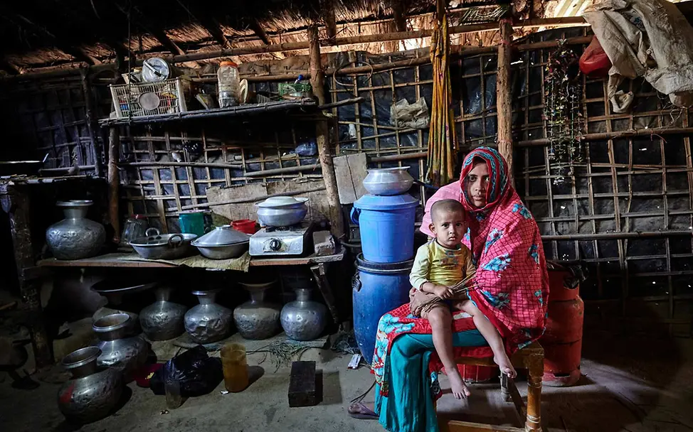 Armut in Bangladesch: Eine Mutter mit ihrem Kind auf dem Schoß in ihrer Küche | © UNICEF/Map Kinderarmut: Eine alleinerziehende Mutter in Bangladesch hält in ihrer Küche ihr Kind auf dem Schoß.