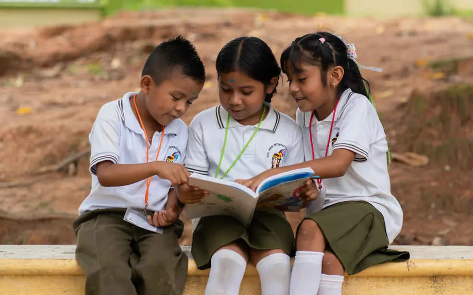 Kinderrechte für Kinder: Alle Kinder sollen lernen und sich entwickeln dürfen – unabhängig von ihrer Herkunft. Kinderrechte leicht erklärt: Drei Schulkinder schauen ein Buch an.