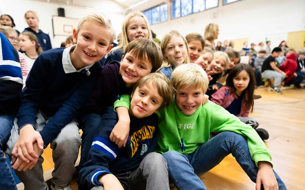 Kinderrechte für Kinder: Kinder haben das Recht, ihre Meinung zu sagen und selbst zu entscheiden. Kinderrechte leicht erklärt: Eine Gruppe Kinder posiert in einer Schulsporthalle.