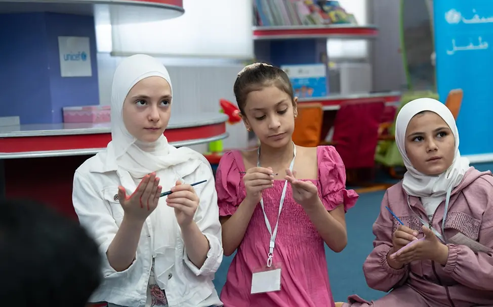 Elizabeth, Aline und Sham nehmen an einer Malaktion teil. | © UNICEF/Dabaan Elizabeth, Aline und Sham nehmen an einer Malaktion in einem kinderfreundlichen Zentrum in Syrien teil.