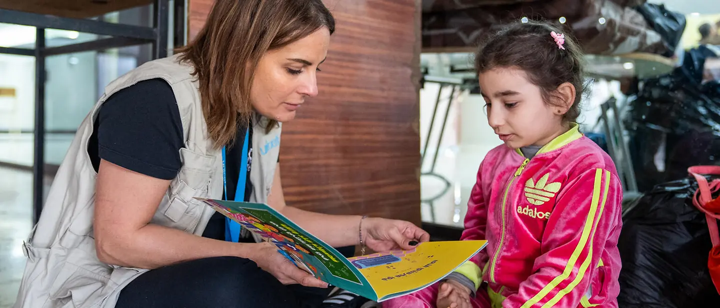Eine UNICEF-Helferin schaut mit einem Mädchen in einer Notunterkunft ein Buch an | © UNICEF/Choufany Libanon spenden: Eine UNICEF-Helferin schaut mit einem Mädchen in einer Notunterkunft ein Buch an