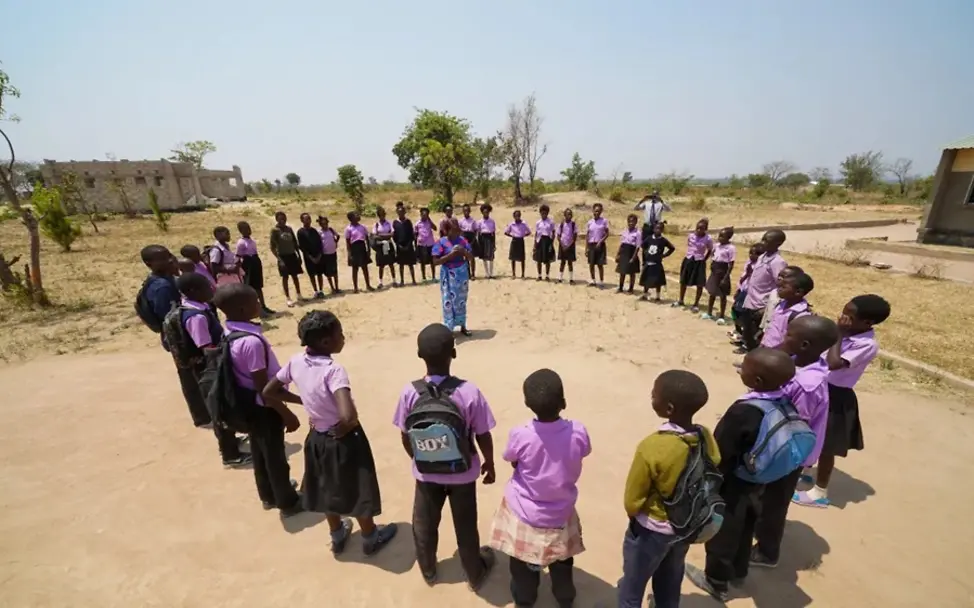 Schüler*innen mit ihrer Lehrerin auf dem Schulhof der Lupili Grundschule. | © UNICEF Zambia/2025/Adam Schüler*innen mit ihrer Lehrerin auf dem Schulhof der Lupili Grundschule.