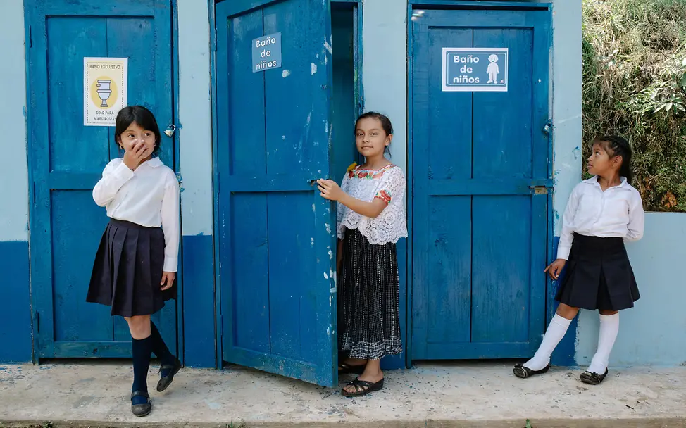Periodenarmut: UNICEF unterstützt den Bau von Toilettenhäusern und Sanitäranlagen in Schulen. | © UNICEF/Lopez Was ist Periodenarmut: Drei Schülerinnen stehen vor den Mädchentoiletten ihrer Schule.