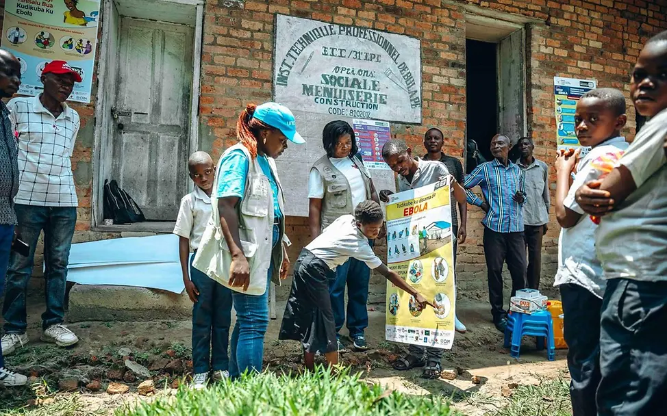 Eine UNICEF-Mitarbeiterin zeigt Kindern ein Poster mit Hygieneschutz-Maßnahmen gegen Ebola. | © UNICEF/Badimu Ebola spenden: Eine UNICEF-Mitarbeiterin zeigt Kindern im Kongo, wie sie sich vor Ebola schützen können.
