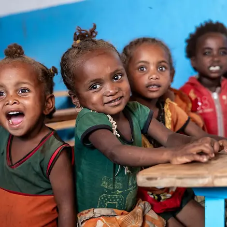 Wirkung: Kinder sitzen gemeinsam an Schulbänken | © UNICEF/Andrianantenaina Wirkung im Klassenzimmer: Mehrere Kinder sitzen an Holzbänken und schauen in die Kamera