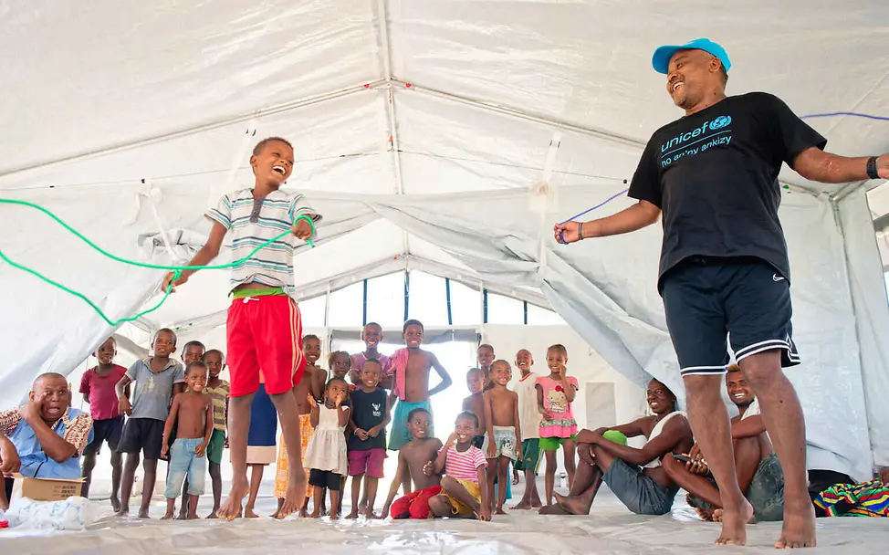 Schule bietet den Kindern nicht nur Bildung, sondern auch eine Struktur im Alltag und die Nähe zu ihren Freund*innen. | © UNICEF/Ramasomanana Folgen von Hochwasser: Ein Junge und ein UNICEF-Mitarbeiter springen Seil im Schulzelt.