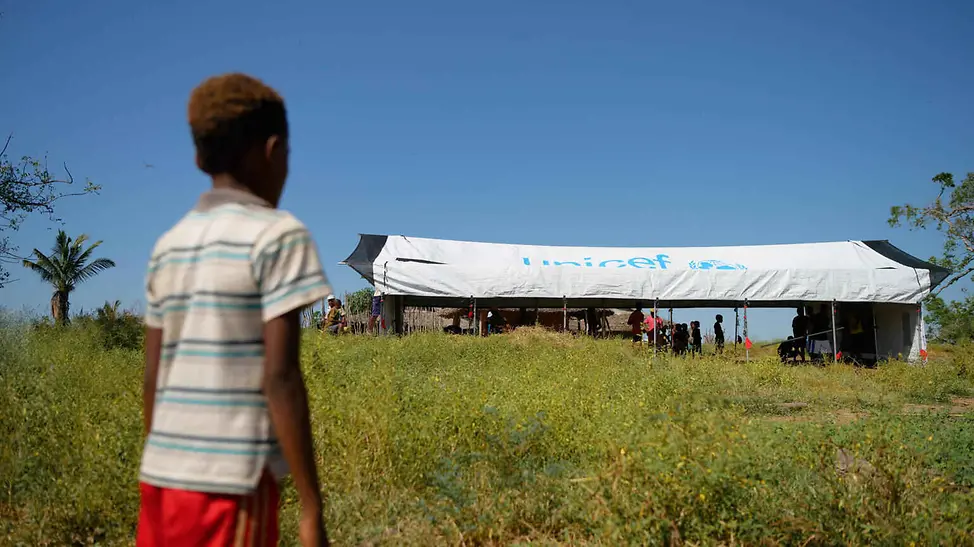 UNICEF baut gemeinsam mit Partnern vor Ort Schulzelte auf und versorgt die Menschen mit dem Nötigsten. | © UNICEF/Ramasomanana Folgen von Hochwasser: Ein Junge schaut beim Aufbau eines UNICEF-Schulzelts zu.