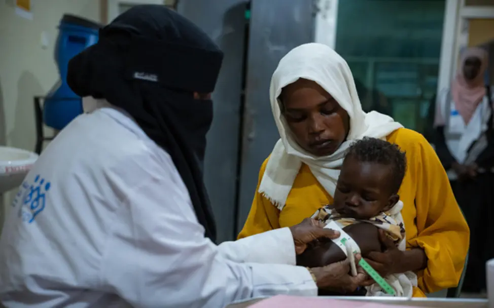 Untersuchung vor Ort: Kind wird in der Klinik betreut | © UNICEF/Elfatih Eine Mutter sitzt mit ihrem Kind, während eine Fachkraft vor Ort eine Messung zur Ernährungsüberprüfung vornimmt.