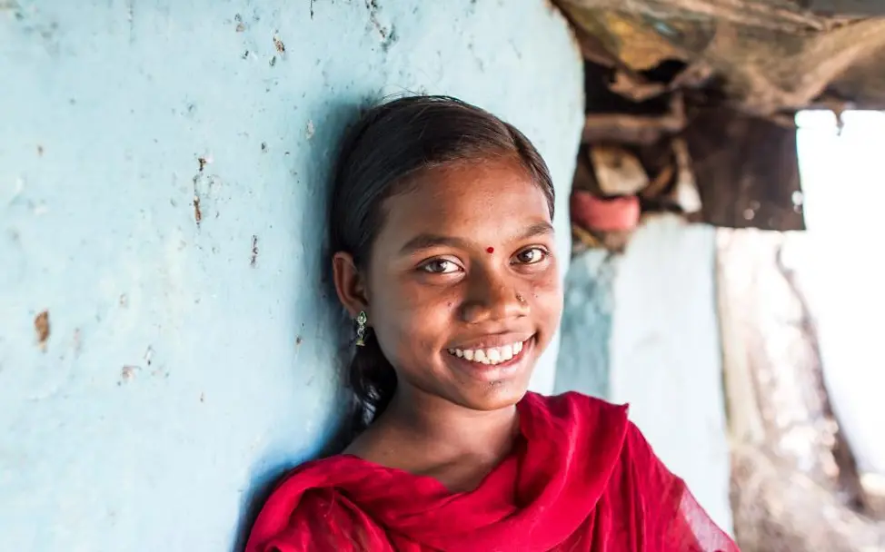 Kinderarbeit Indien: Ein Mädchen kann dank UNICEF und Nichtregierungsorganisationen wieder zur Schule gehen. | © UNICEF India /Singh Kinderarbeit: Die 14-jährige Vaishali lehnt lächelnd an einer blauen Wand.
