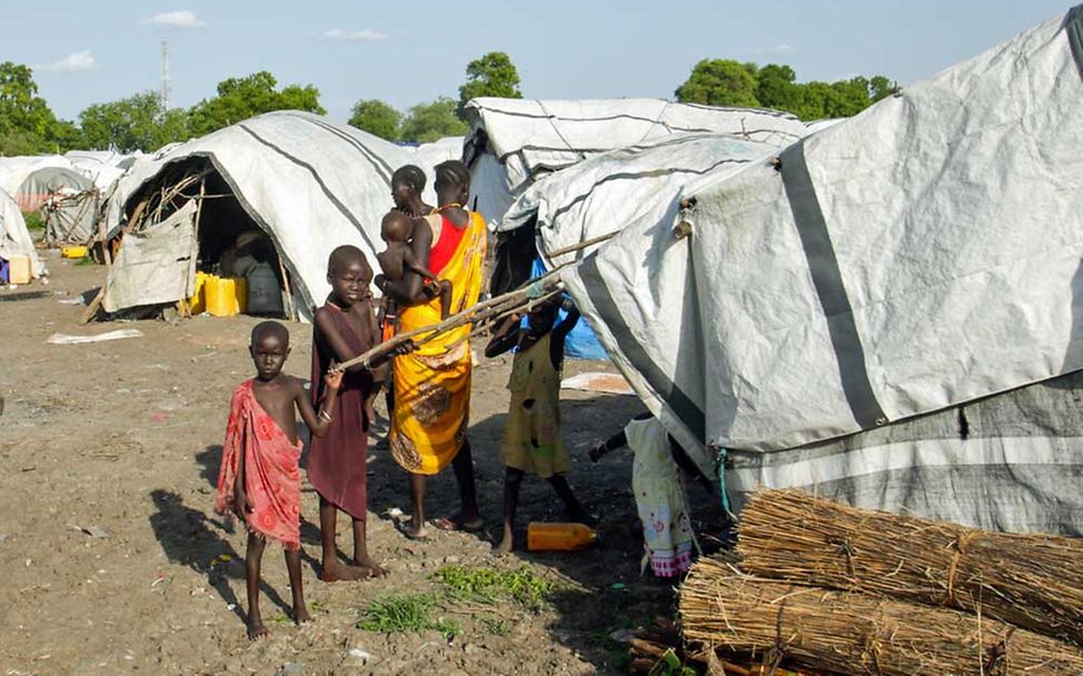 Nothilfe Südsudan: Eine südsudanesische Familie steht in einem Flüchtlingslager unter einer Zeltplane