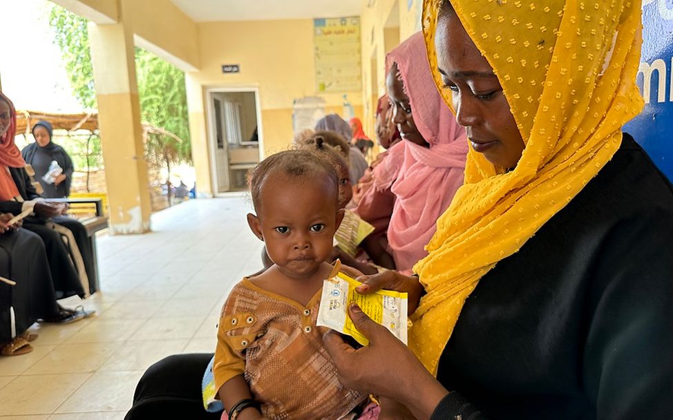 Sudan: Ein Kind sitzt auf dem Schoß seiner Mutter und wird gefüttert