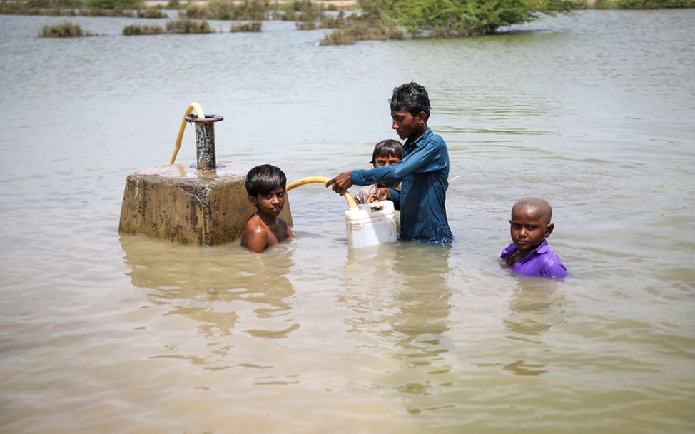 Kinder versuchen Trinkwasser aus einer überfluteten Wasserpumpe zu retten.