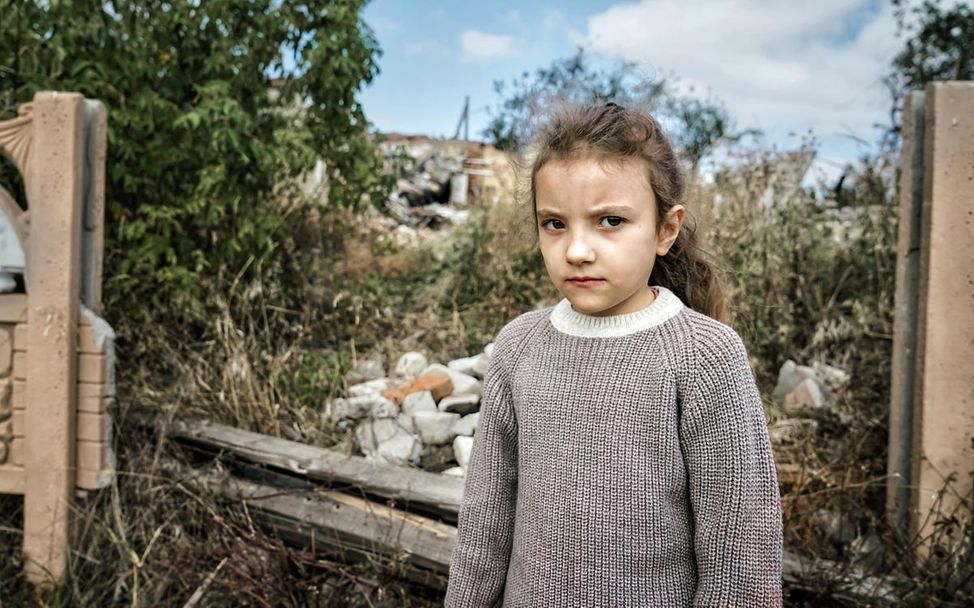 Kinder im Ukraine-Krieg: Ein Mädchen in der Charkiw-Region steht vor einer durch einen Luftangriff zerstörten Schule.