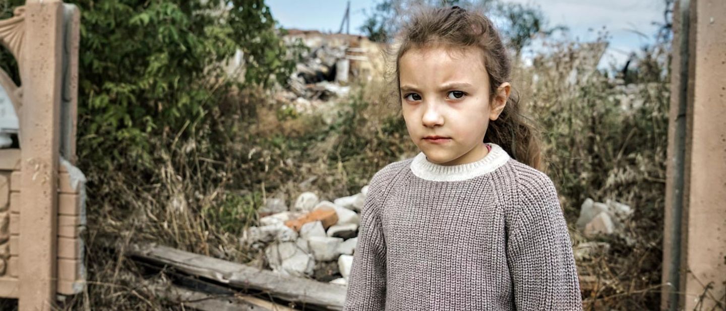 Spenden Ukraine: Ein Mädchen in der Charkiw-Region steht vor einer durch einen Luftangriff zerstörten Schule.