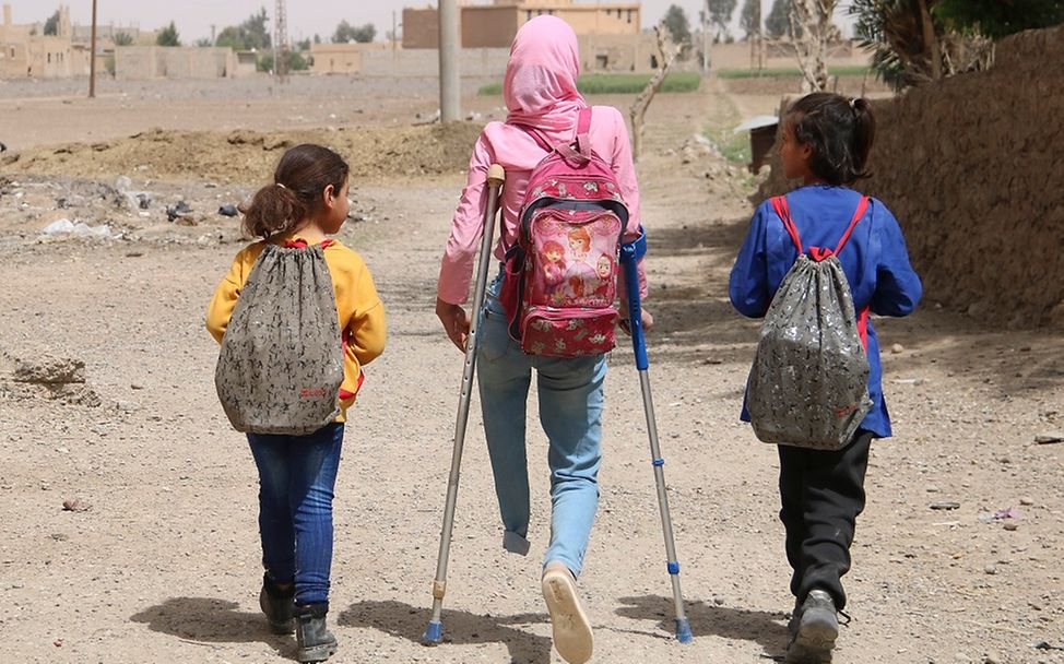 Kinder im Krieg: Ein Mädchen in Syrien geht auf Krücken mit Schulkameraden einen Weg entlang