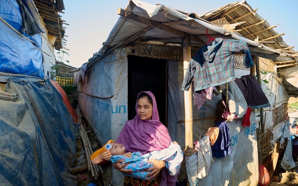Weltflüchtlingstag: Ein Porträt einer jungen Mutter mit ihrem Baby vor ihrer Hütte im Rohingya-Flüchtlingslager